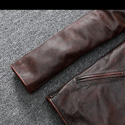 Detalle de una campera de cuero de vacuno marrón con cierre en el puño, sobre superficie gris texturizada.