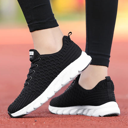 Mujer usando zapatillas deportivas negras ligeras y transpirables con suela blanca en pista roja.