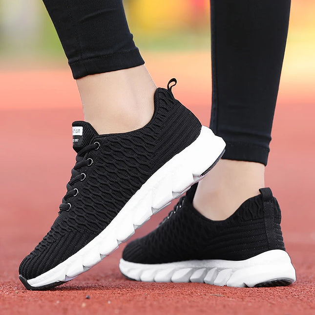 Mujer usando zapatillas deportivas negras ligeras y transpirables con suela blanca en pista roja.