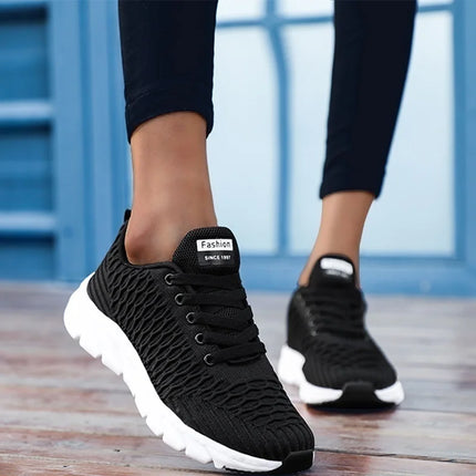 Black lightweight breathable women's athletic sneakers on a wooden floor, showcasing style and comfort.