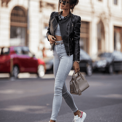 Mujer con campera de cuero negra, jeans ajustados y bolso beige caminando en la ciudad, reflejando estilo urbano y moderno.
