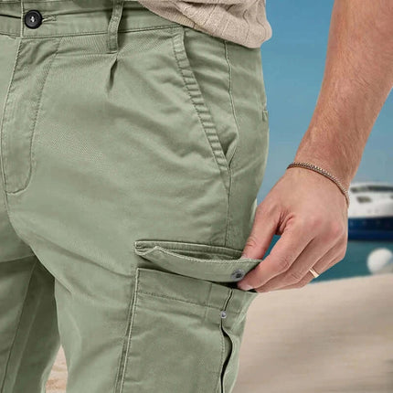 Close-up of a person wearing versatile green cargo pants with a side pocket on a beach, showcasing the pants' practical features.
