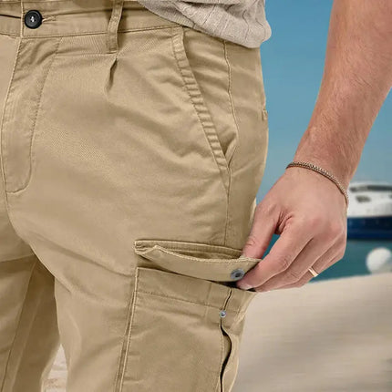 Close-up of beige cargo pants with side pocket buttoned on a sunny beach background.