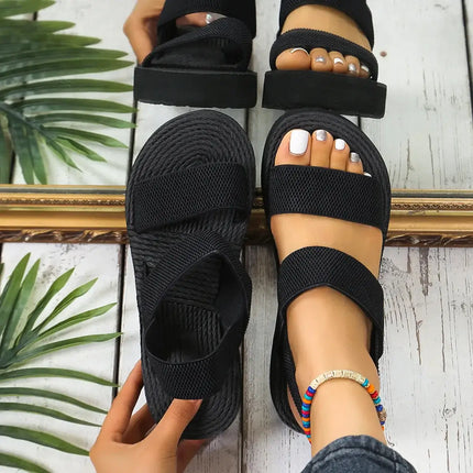 Woman wearing black ComfortFlex sandals with ankle strap for style and comfort, reflected in a mirror on wooden floor.