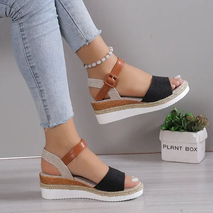 Stylish women's wedge sandals with brown strap, black and beige design, paired with light denim jeans, showcasing elegance and comfort.