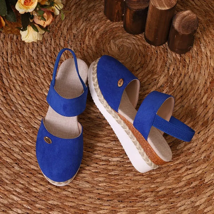 Blue wedge sandals with closed toe and adjustable strap on woven mat background.