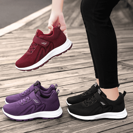 Three pairs of Zapatillas ComfyRun in red, purple, and black placed on a wooden floor, showcasing lightweight and breathable design.