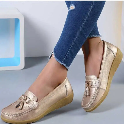 Alt Tag: Mujer usando zapatillas tipo mocasín doradas con detalle metálico, elegantes y cómodas, sobre un suelo gris.