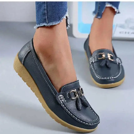 Mujer luciendo zapatillas tipo mocasín Alba, elegantes y cómodas, en material sintético con acabado cuero y detalle metálico.