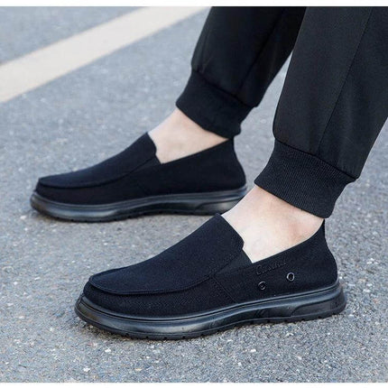 Zapatos de lona casuales negros para hombre, ideales para caminar, fotografiados en uso sobre pavimento.