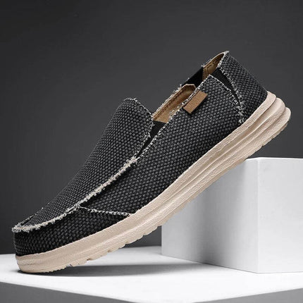 Zapatos casuales hombre transpirables de lona en negro sobre fondo gris, estilo moderno y cómodo ideal para cualquier ocasión.